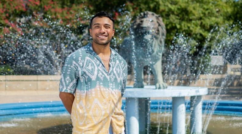 Photo of a man standing in front of a statue and a fountain. 